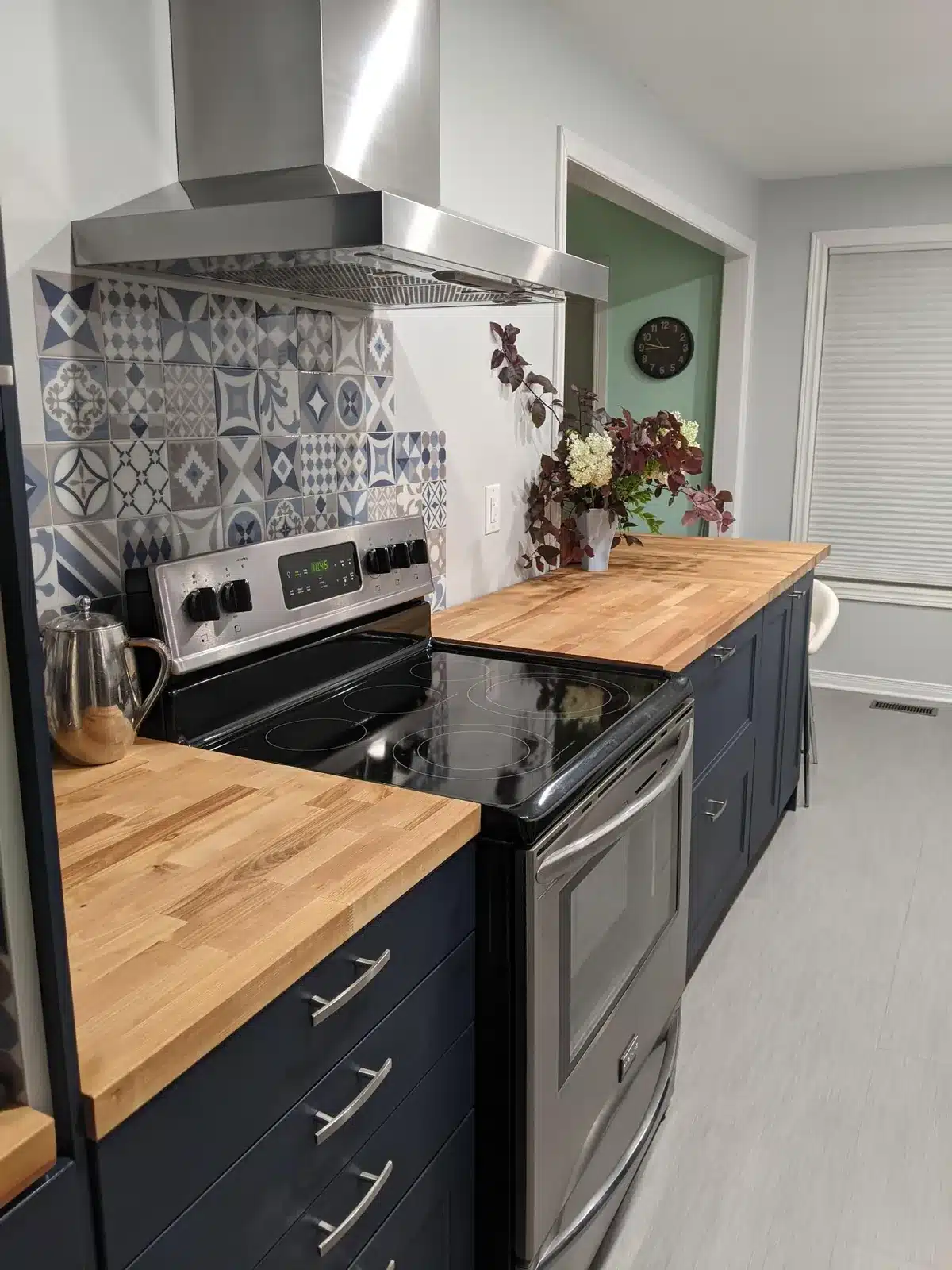 IKEA AXSTAD blue kitchen with butcher block counters, a stainless chimney hood and patterned tile backsplash