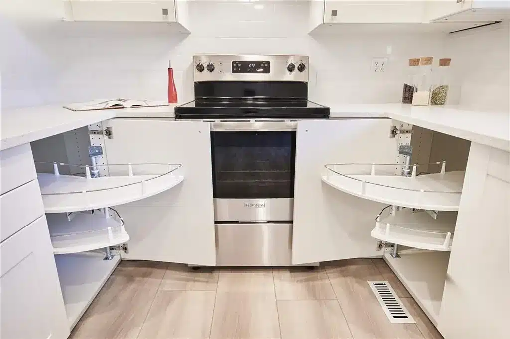 IKEA AXSTAD matt white corner base cabinets open to show carousel shelves on both sides of the range